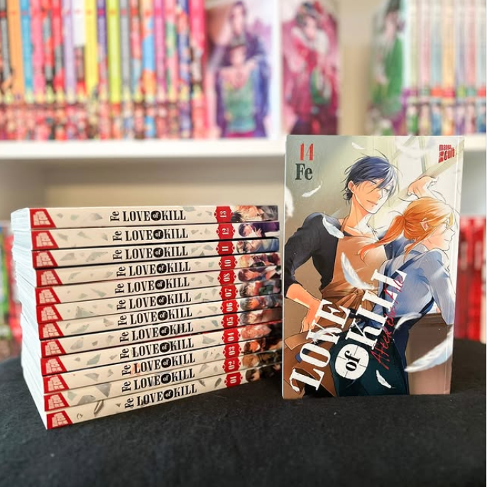 Im Hintergrund: Buchregal mit Manga. Im Vordergrund: Auf einem Tisch sind alle Bände der Manga-Serie Love of Kill aufeinander gestapelt. Angelehnt daran ist der Letzte Band, Band 14.