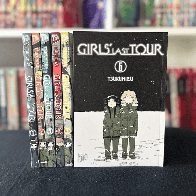 Sechs Bände der Manga-Serie „Girls’ Last Tour“ von Tsukumizu, aufgereiht in einem Regal. Band 6 ist prominent im Vordergrund platziert und zeigt zwei Figuren in Winterkleidung vor einer verschneiten Landschaft.